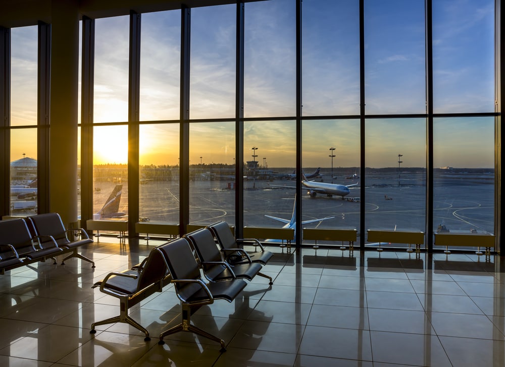 Silhouettes of bench in interior in airport lounge on background of the airfield with passenger planes