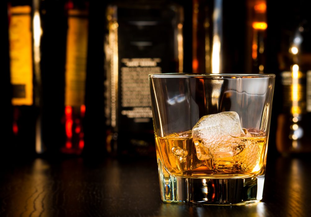 A glass of whiskey on the rocks on a dimly lit bar to celebrate world whiskey day.