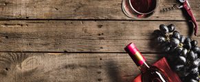 Glass of red wine, grapes, and wine opener on rustic wooden table.