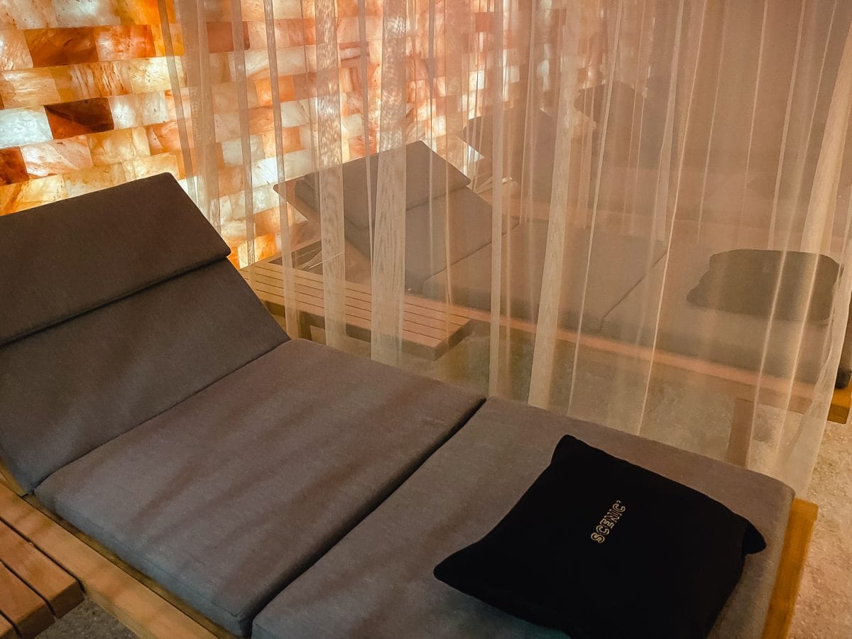 a brown chaise lounge in a salt room with crush salt on floor and blocks of himalyan salt on walls, a gauzy drape provides privacy