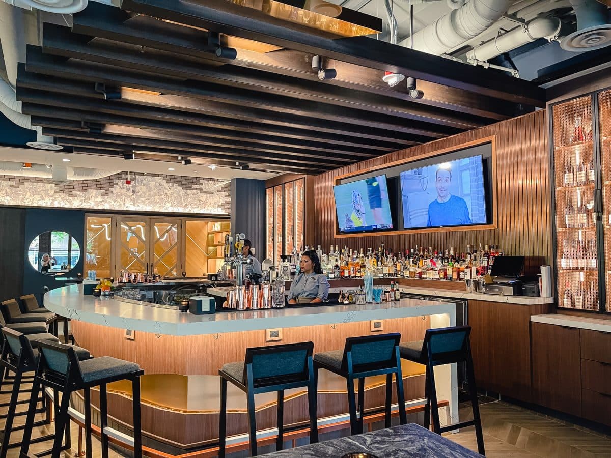 industrial bar with chair surrounding a bar back and televisions on the wall