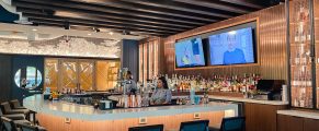 industrial bar with chair surrounding a bar back and televisions on the wall