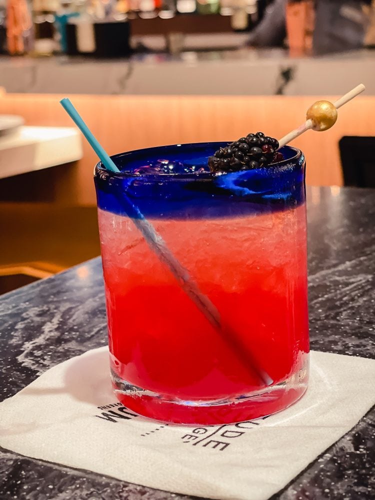 bright pink specialty cocktail in glass with straw and blackberry garnish