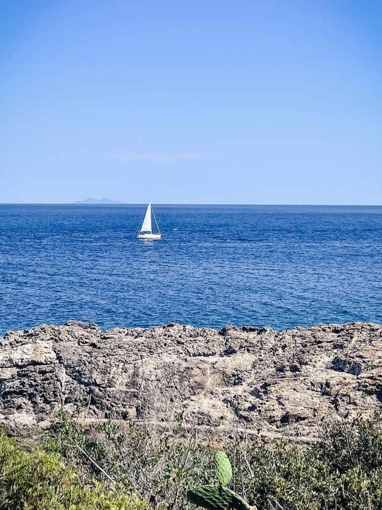 sailboat in the blue water off a rocky coast of elba