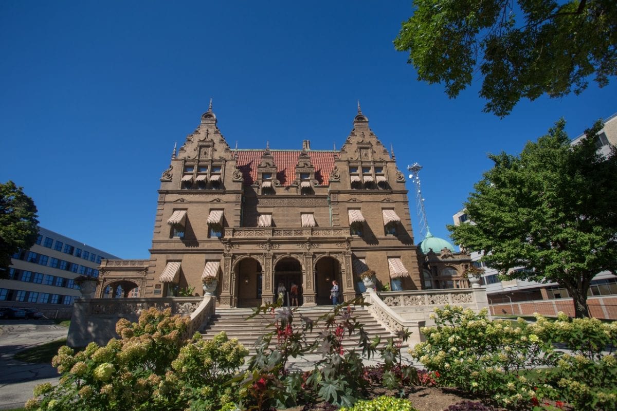 exterior shot of the pabst mansion in milwaukee, a historic brick building with steps leading up to it, surrounded by a garden in bloom