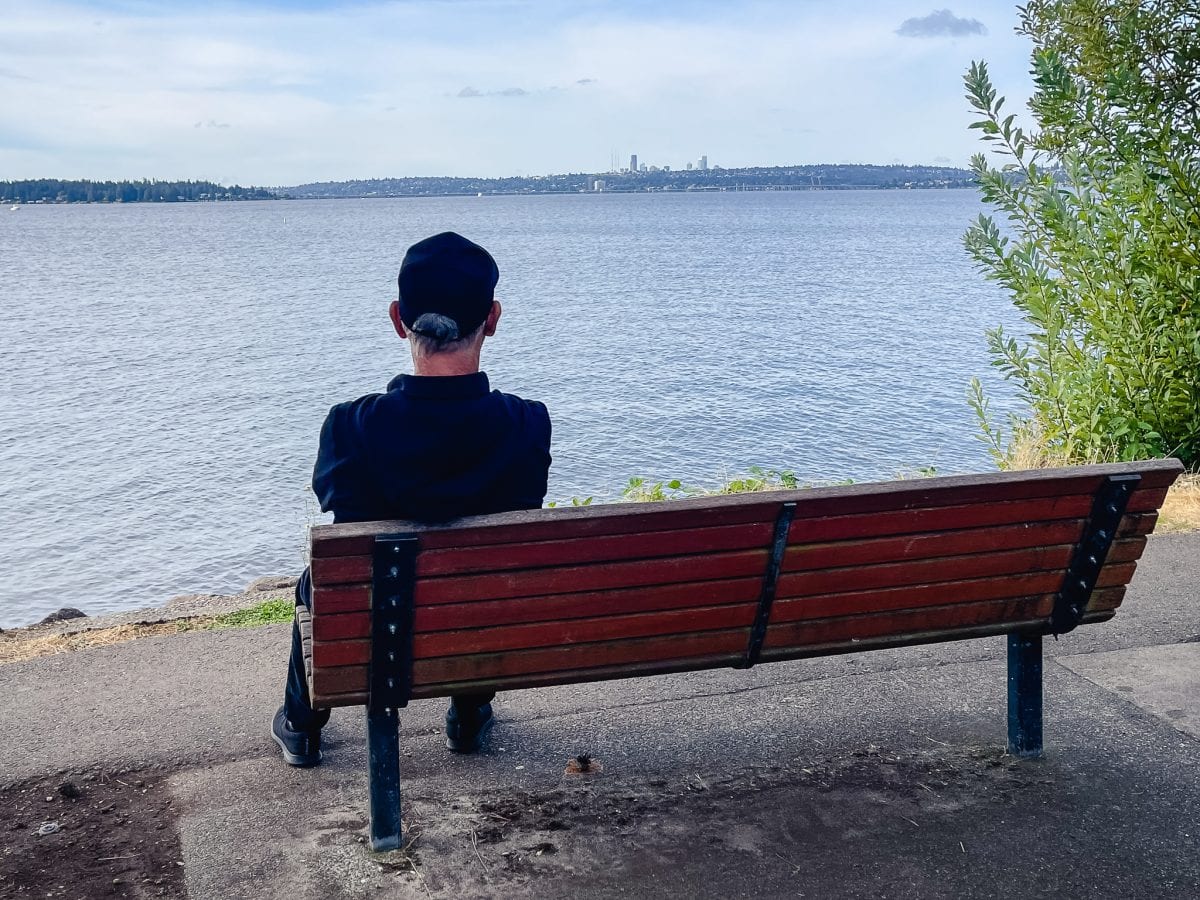 a man sitting on a bench and looking out over lake washington at downtown seattle