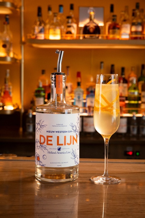 a bottle of holland america de lijn gin and a cocktail served in champagne flute