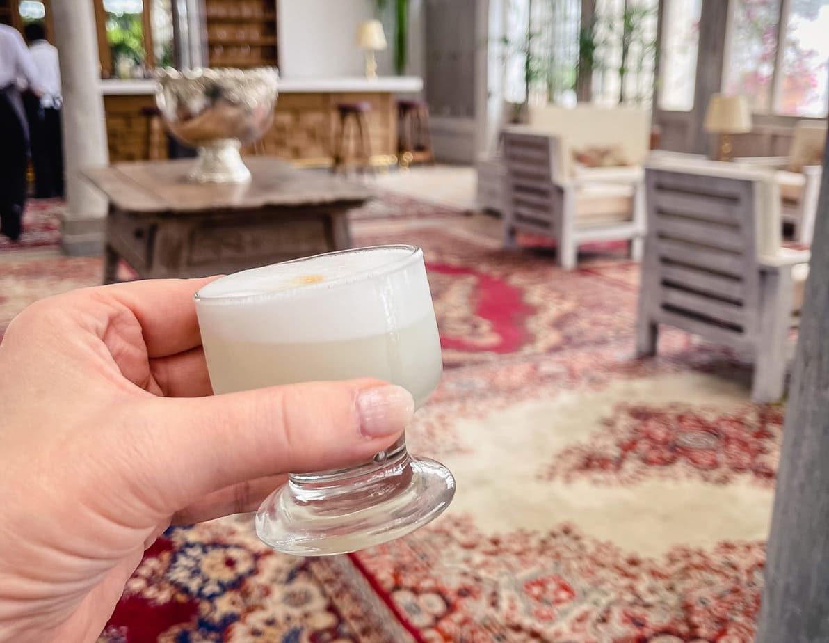 a pisco sour held against a backdrop of a peruvian living room