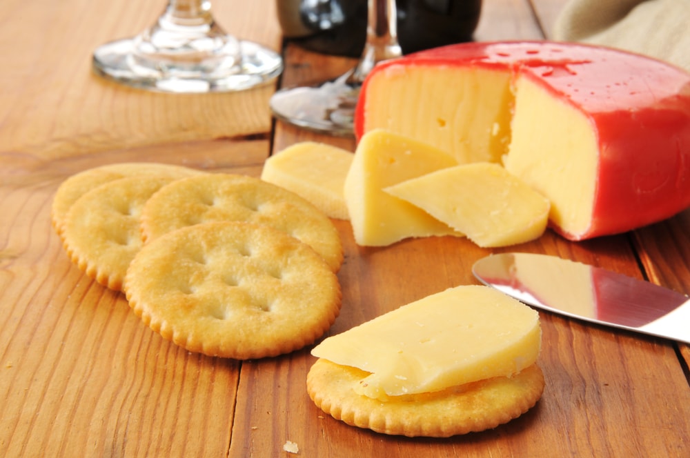 sliced gouda cheese on crackers with wine glasses.  shallow depth of field.