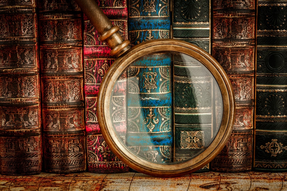 photo of a book shelf with vintage volumes on it and a magnifying glass in front