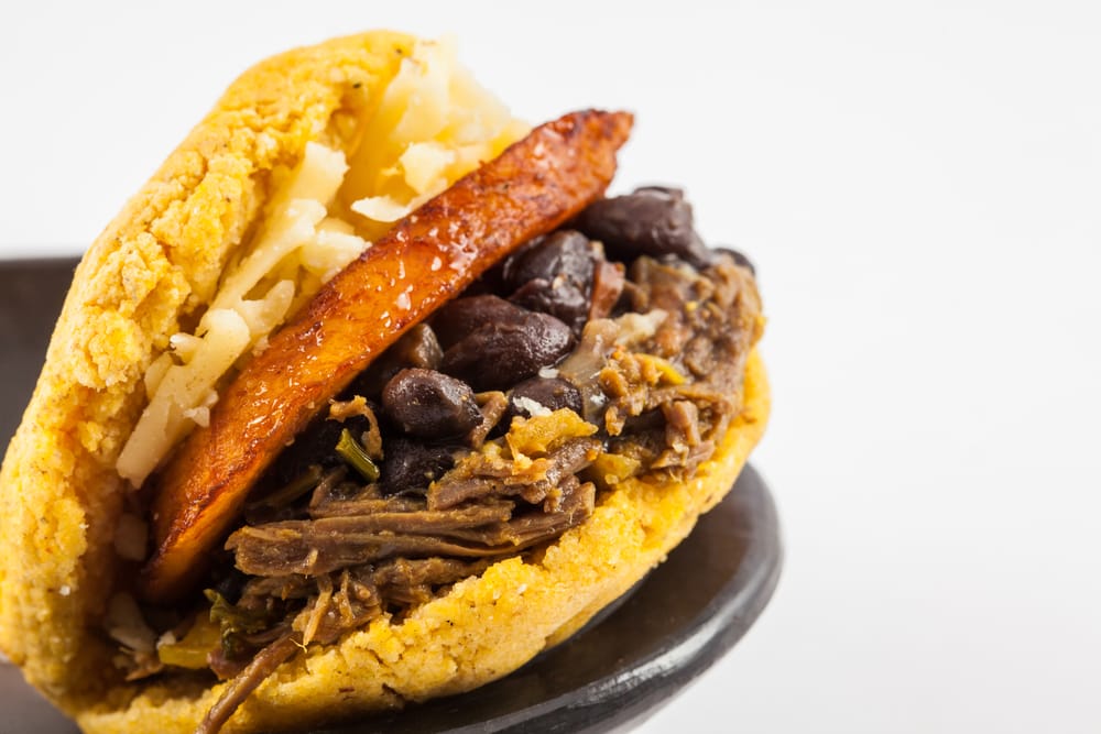 Arepas filled with shredded beef, black beans, plantain and cheese served in a black ceramic dish on white background