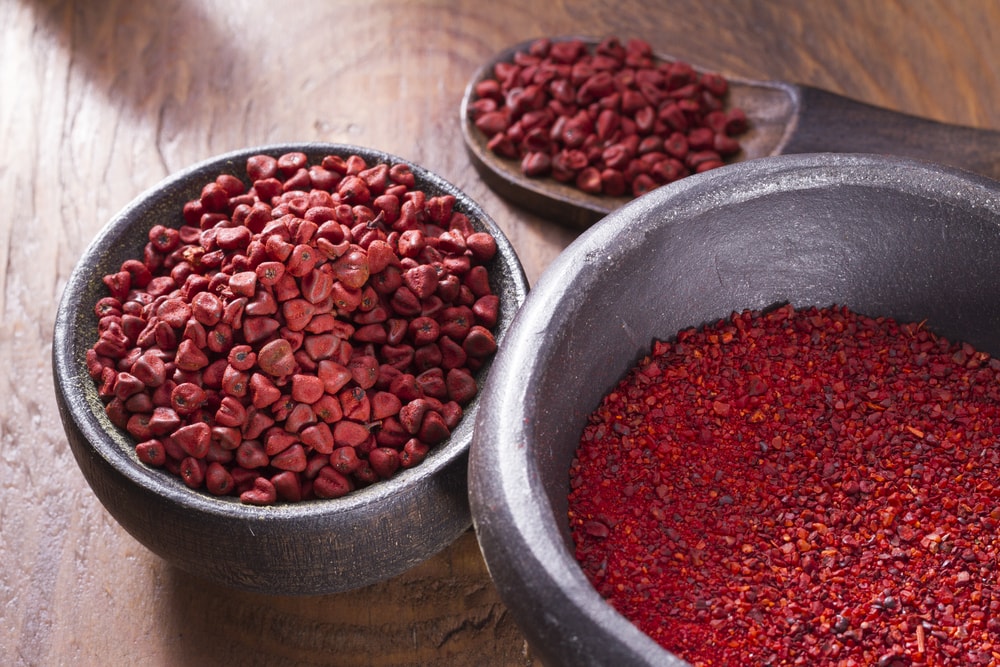 Annatto beans in bowl on wooden table.