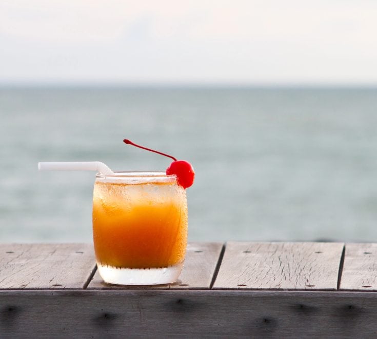 a glass of barbados rum punch with ocean in background