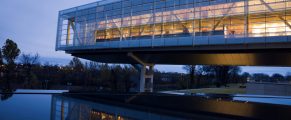 Modern glass building featuring illuminated interior at dusk.