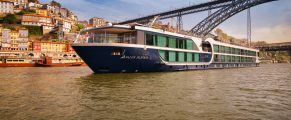 Luxurious river cruise ship sailing in Porto, Portugal with colorful hillside buildings and Dom Luís I Bridge in background.