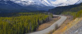 Snow-capped mountains and winding mountain road in Alaska wilderness.