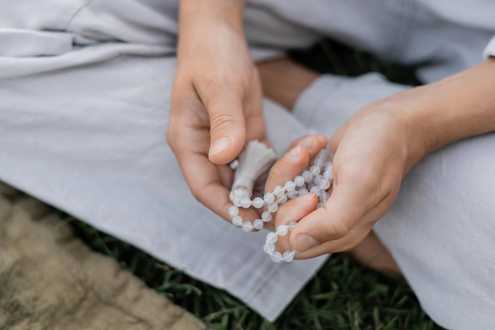 A person sitting on the grass and meditating with mala beads in their hands.