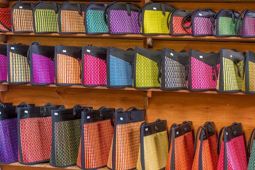 A shelf with many different colored cambodia woven straw bags on it.