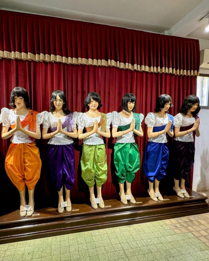 A row of mannequins in colorful sampots standing in front of a curtain.
