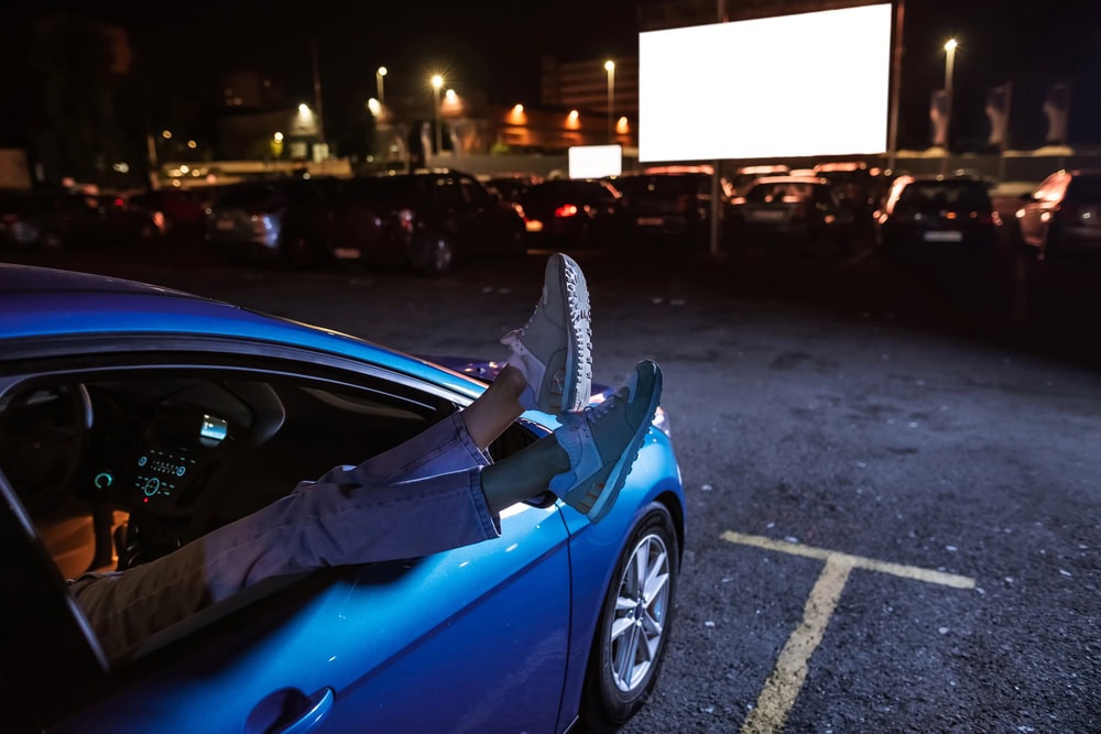 Young girl hanging her legs out of car window while watching a movie at drive in cinema from the front seat of the car
