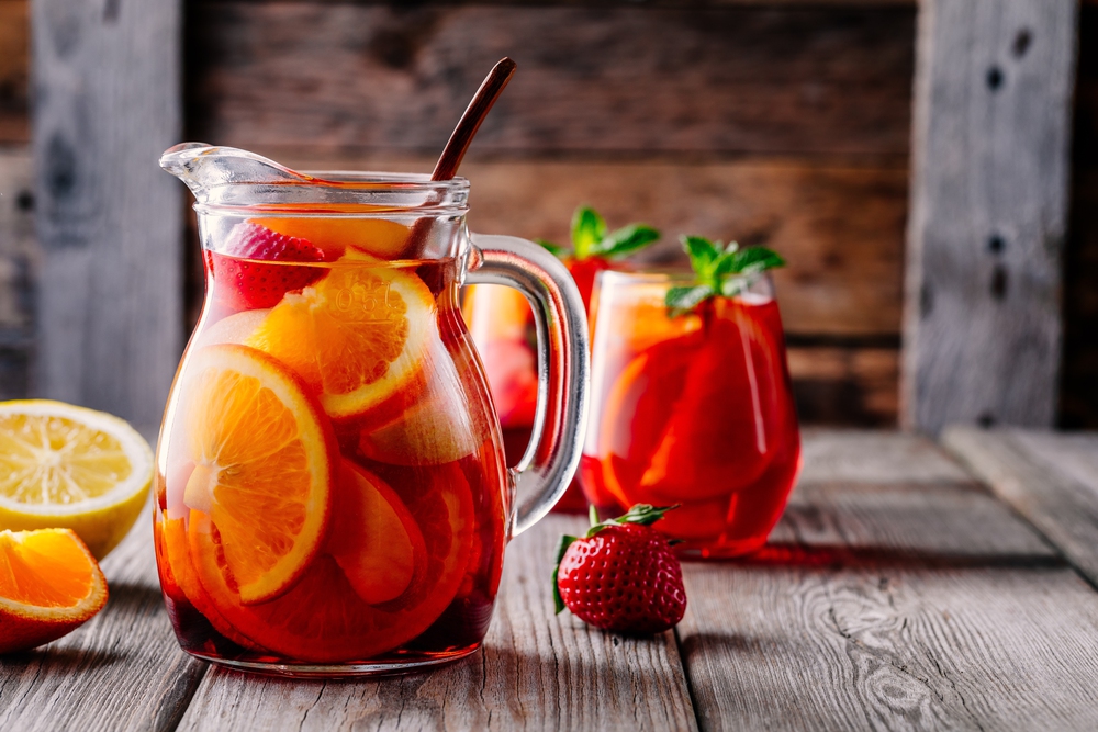 Discovering Sangria in Spain 1 Homemade red wine sangria with orange, apple, strawberry and ice in pitcher and glass on rustic wooden background