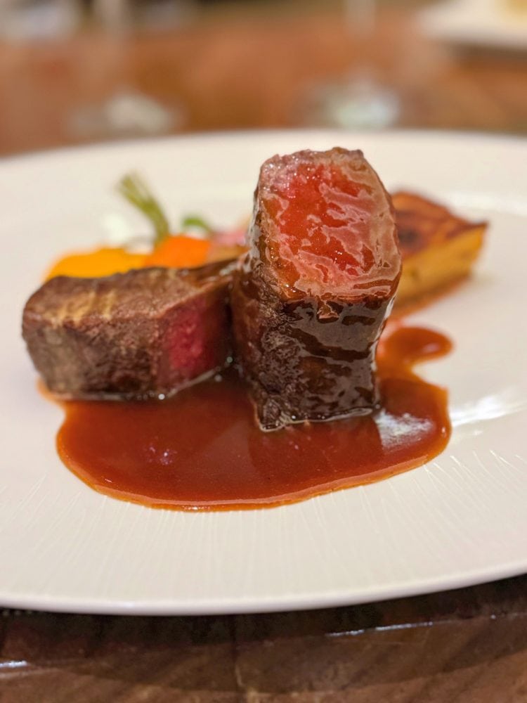 Gourmet beef tenderloin with red wine sauce on a white plate.