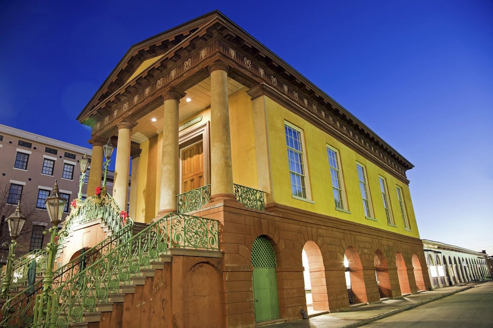 12 Terrific Museums in Charleston to Put on Your To-Visit List 6 Historic yellow Charleston museum with green staircase and arches at twilight.